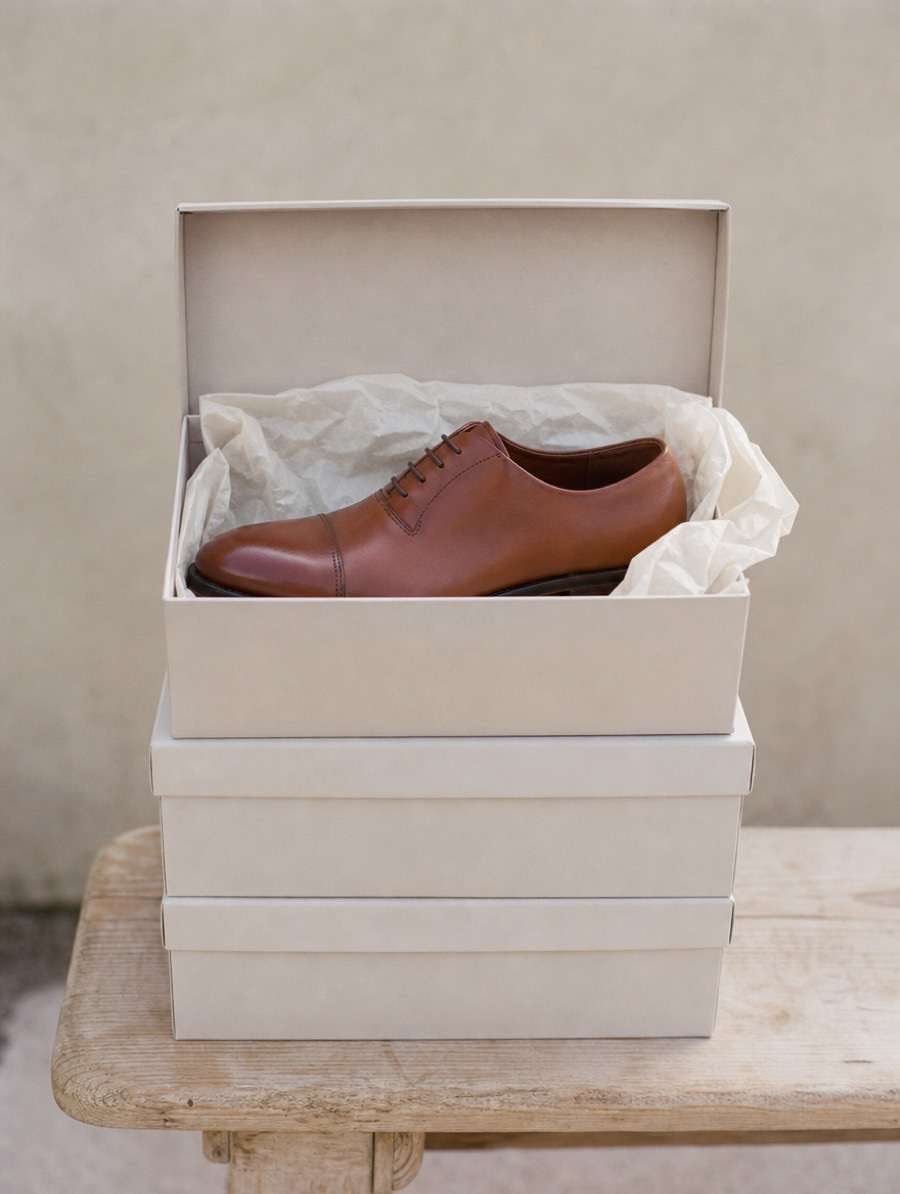 Gros plan de boîtes à chaussures empilées, celle du dessus ouverte laissant voir le papier de soie et une chaussure en cuir.